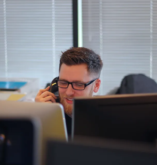 Muškarac sjedi u uredu za stolom i razgovara na telefon.